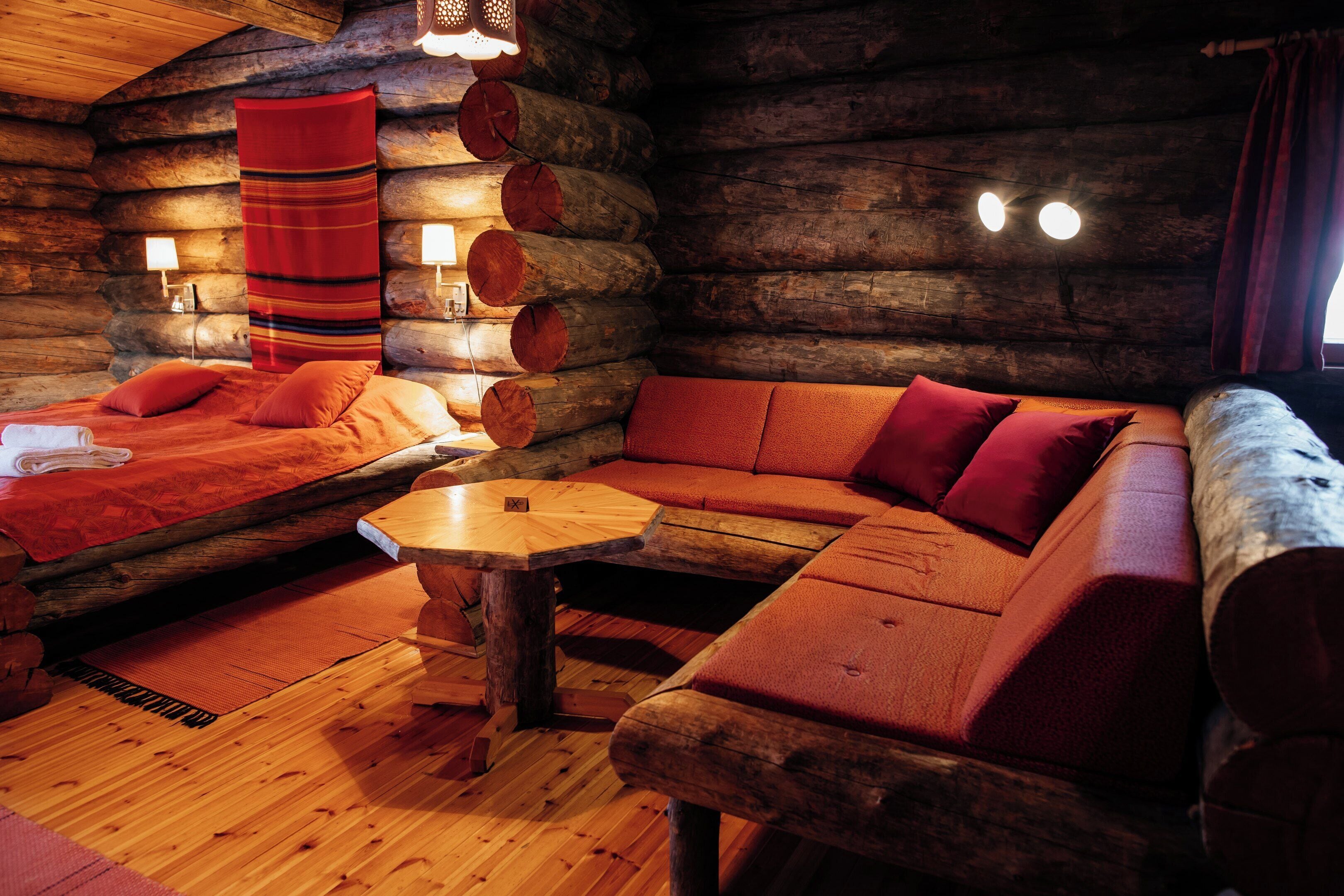 A cozy log cabin interior with a sofa, a small table, and a bed with red bedding.