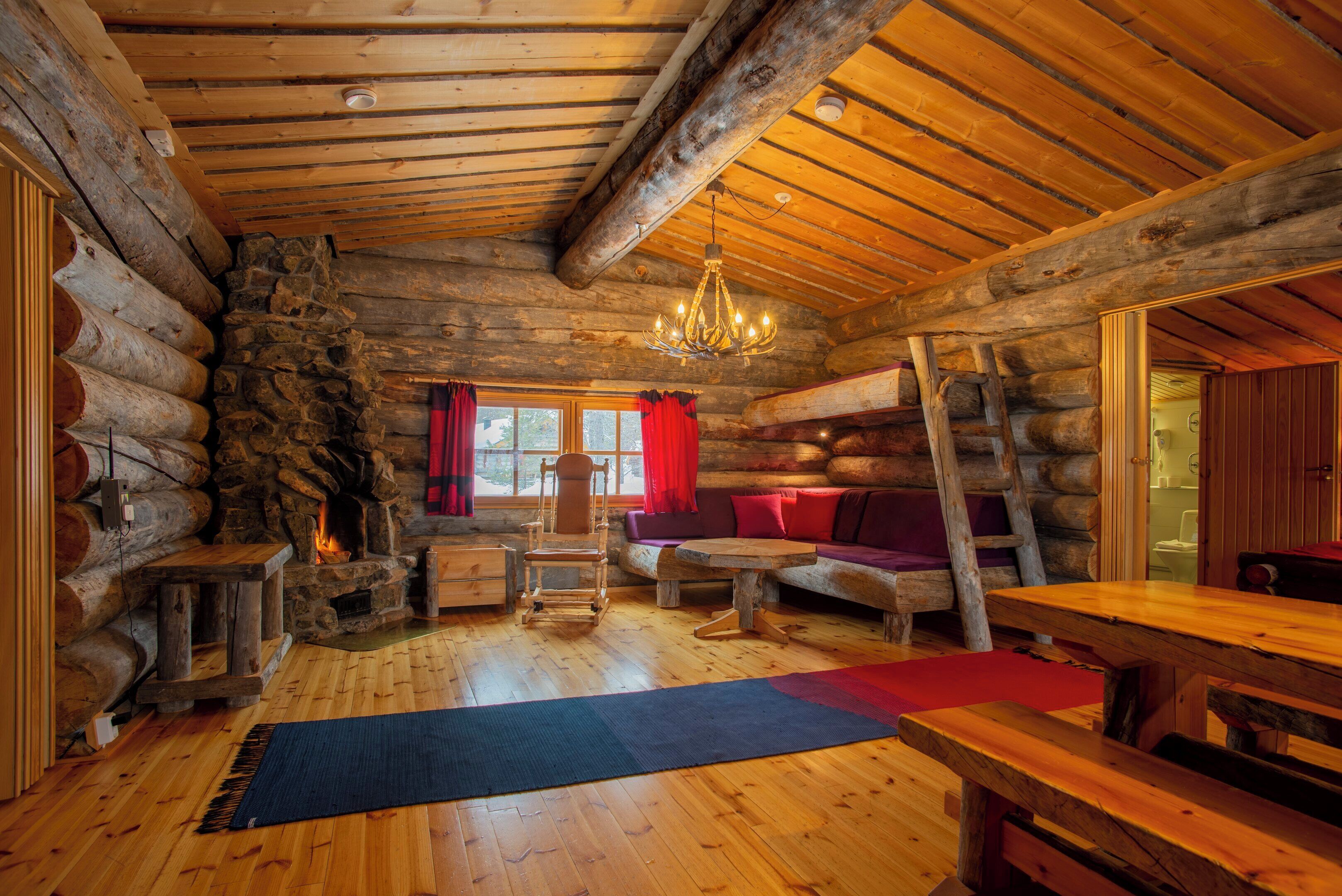 L’intérieur d’une cabane en rondins, avec une cheminée en pierre, des meubles en bois et un lustre.