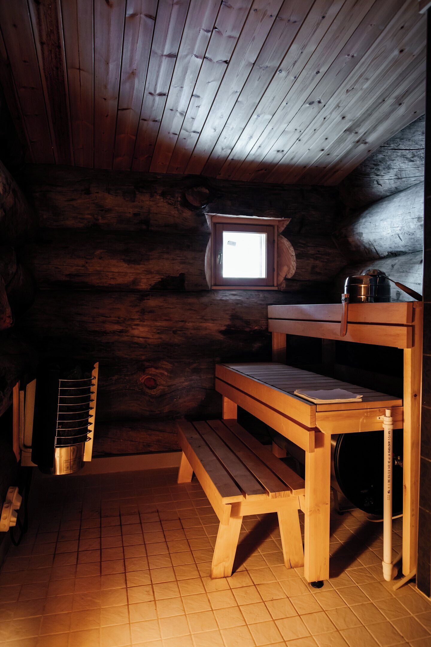 A cabin with a wooden interior, a window, a bench, and a kettle.