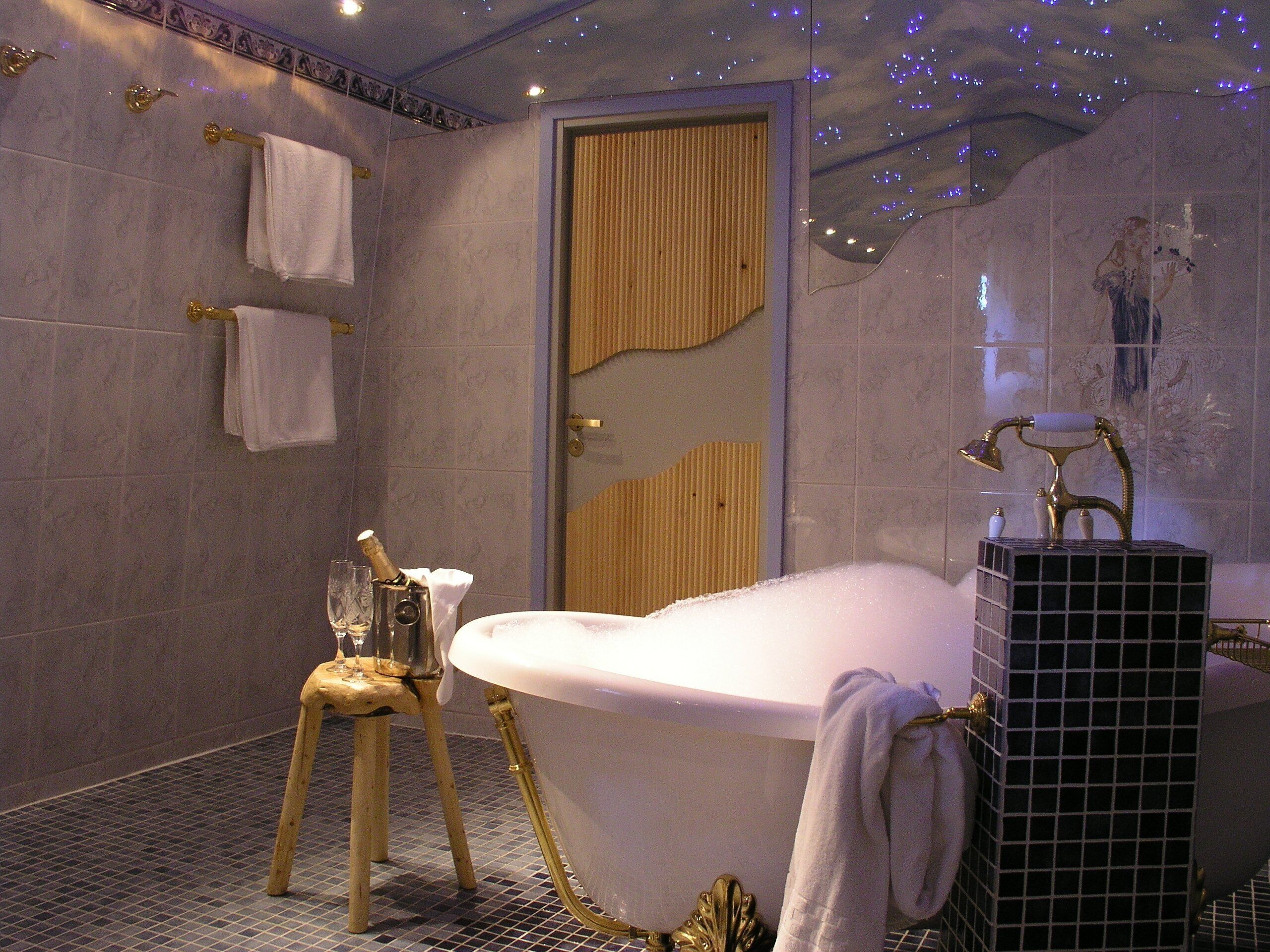 Un baño con una bañera grande, un taburete de madera y una zona de ducha decorativa.