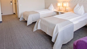 Habitación de hotel con dos camas individuales, suelo alfombrado, pared con diseño y una puerta que da a otra habitación.