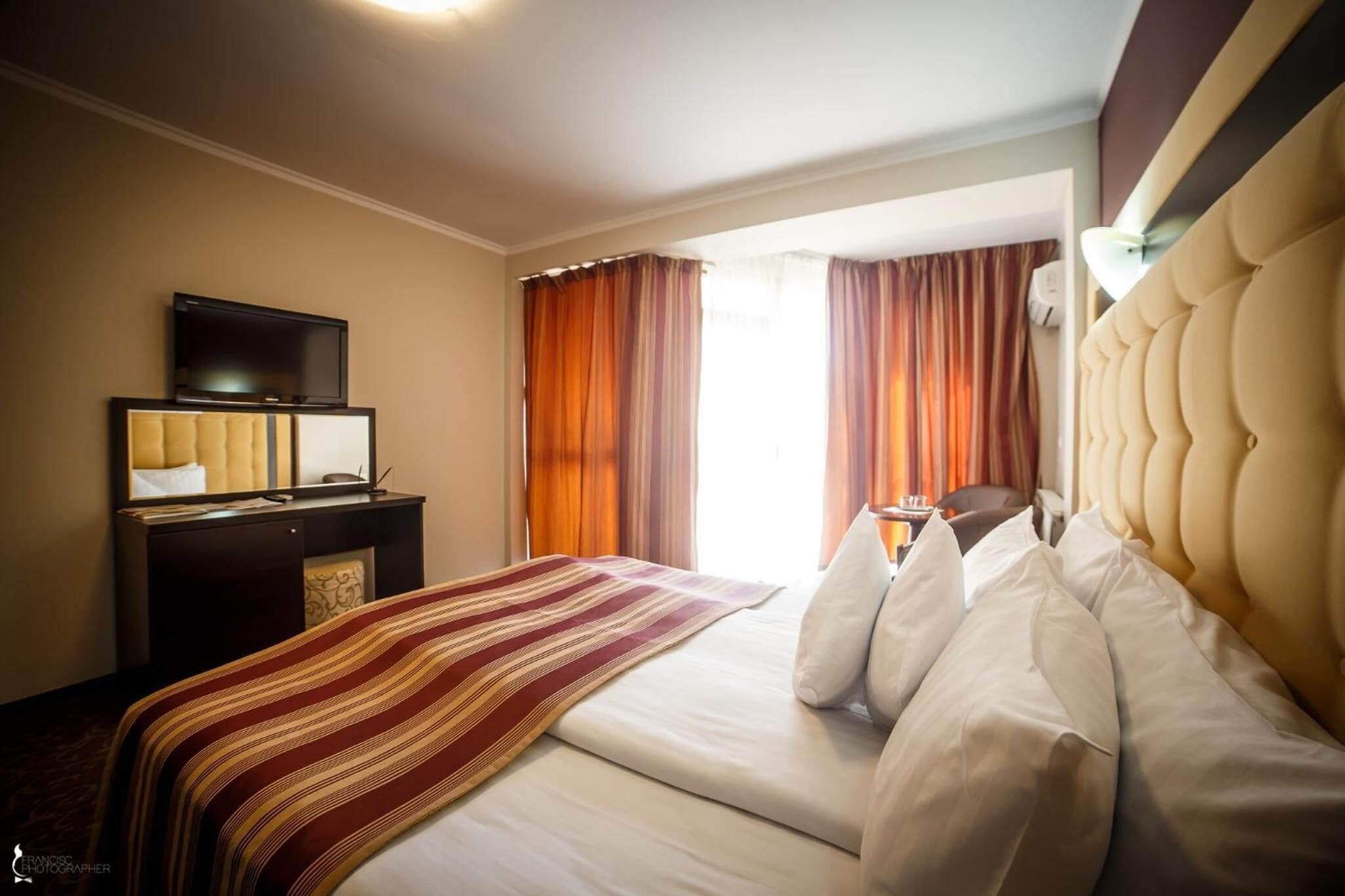 A hotel room with a bed, a desk with a television, and a window with curtains.