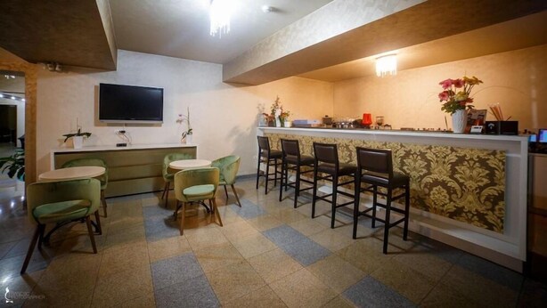 A restaurant with a bar area, green chairs, a flat-screen TV, and a patterned wallpaper on the wall. - Ozana (Bistri?a)