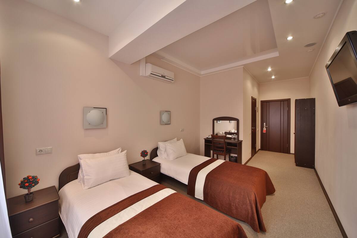 Een hotelkamer met twee bedden, een bureau, een stoel, een televisie en een airconditioner.