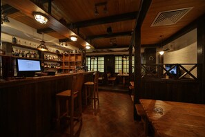 Zona de bar con muebles de madera, estantes con botellas y un monitor de ordenador.