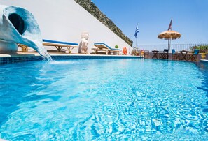 A swimming pool with a water slide, lounge chairs, and flags.