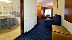 A hotel room with a bathroom, a seating area, and a view of the outside.