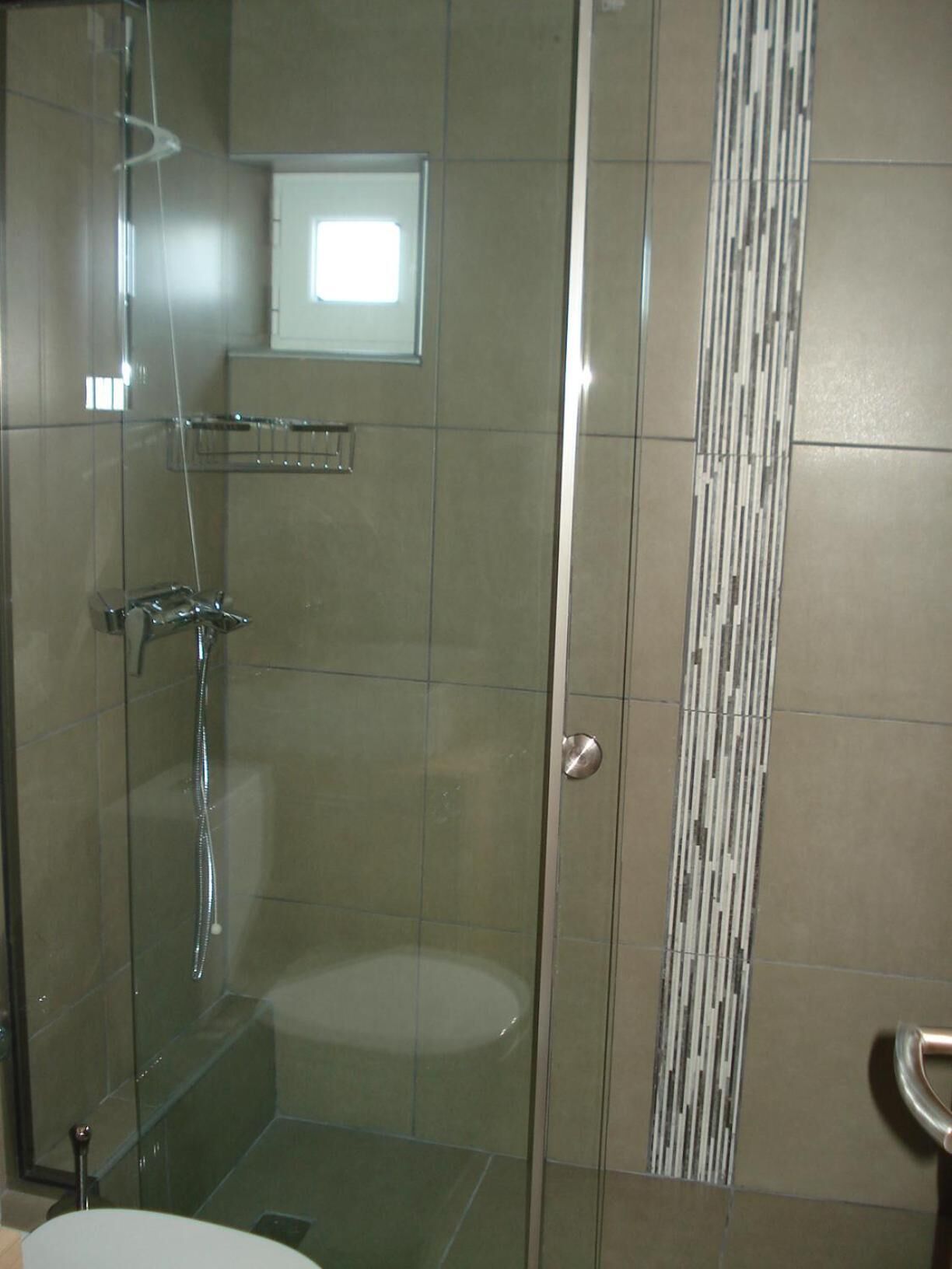 A glass-enclosed shower stall with a handheld showerhead and a wall-mounted faucet.