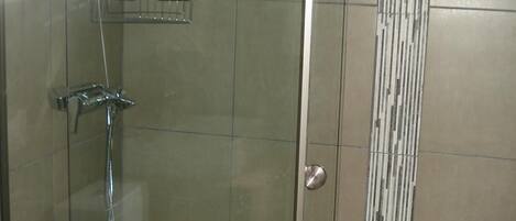 A glass-enclosed shower stall with a handheld showerhead and a wall-mounted faucet.