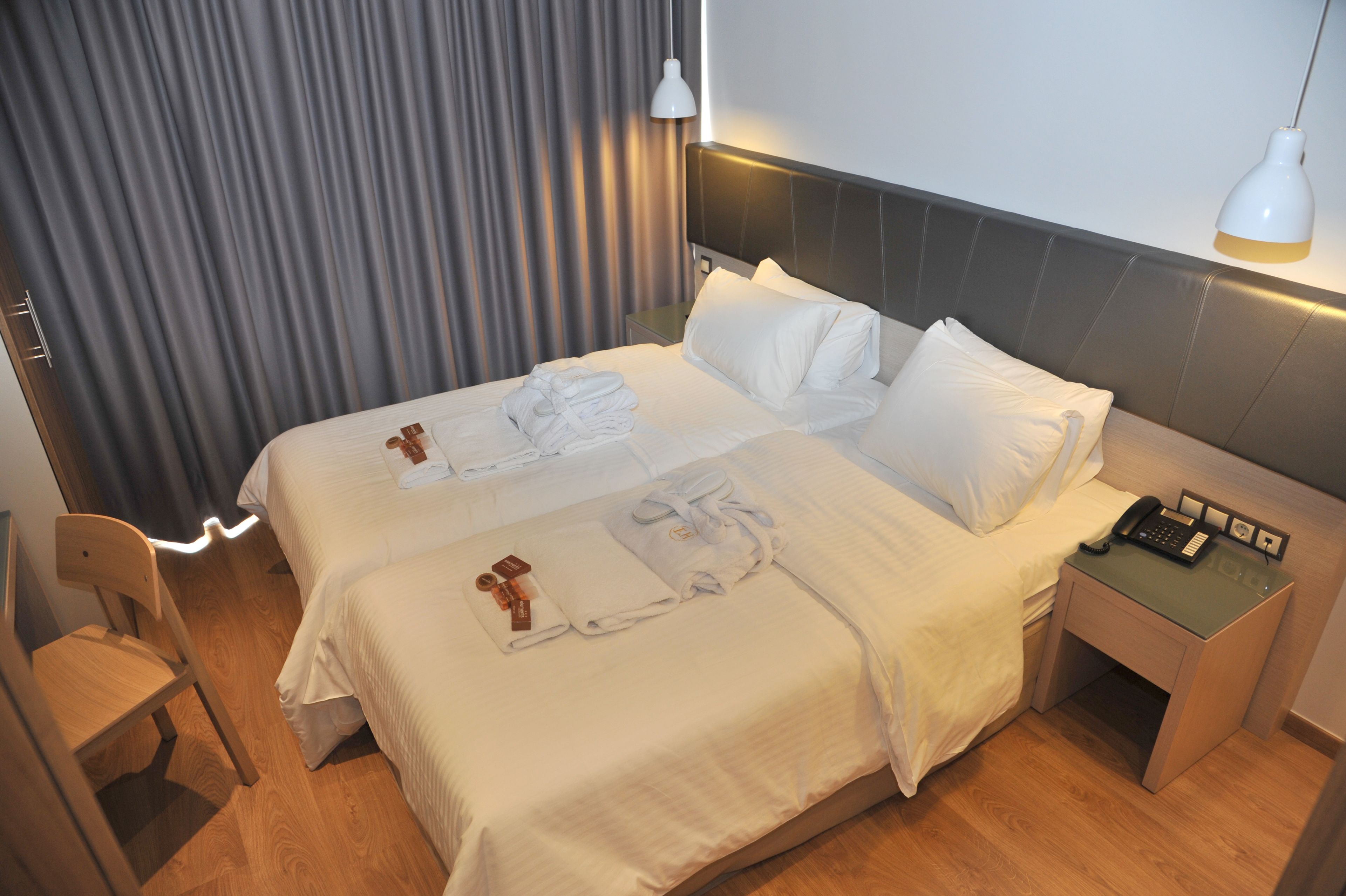 Een hotelkamer met twee bedden, een nachtkastje met een telefoon en een stoel.