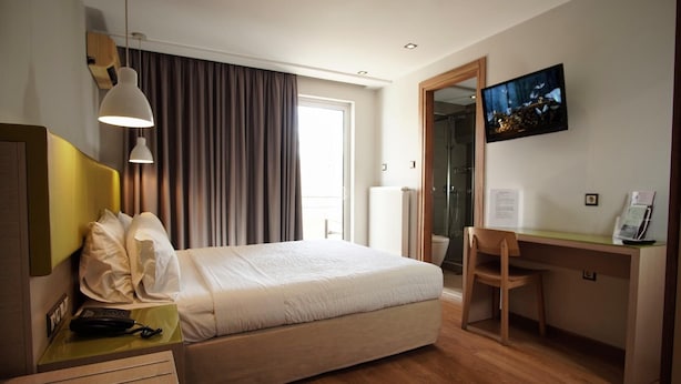 A hotel room with a bed, a desk, a chair, a telephone, a television, and a window with curtains. - Elements Rooms and Apartments (Chalandri)