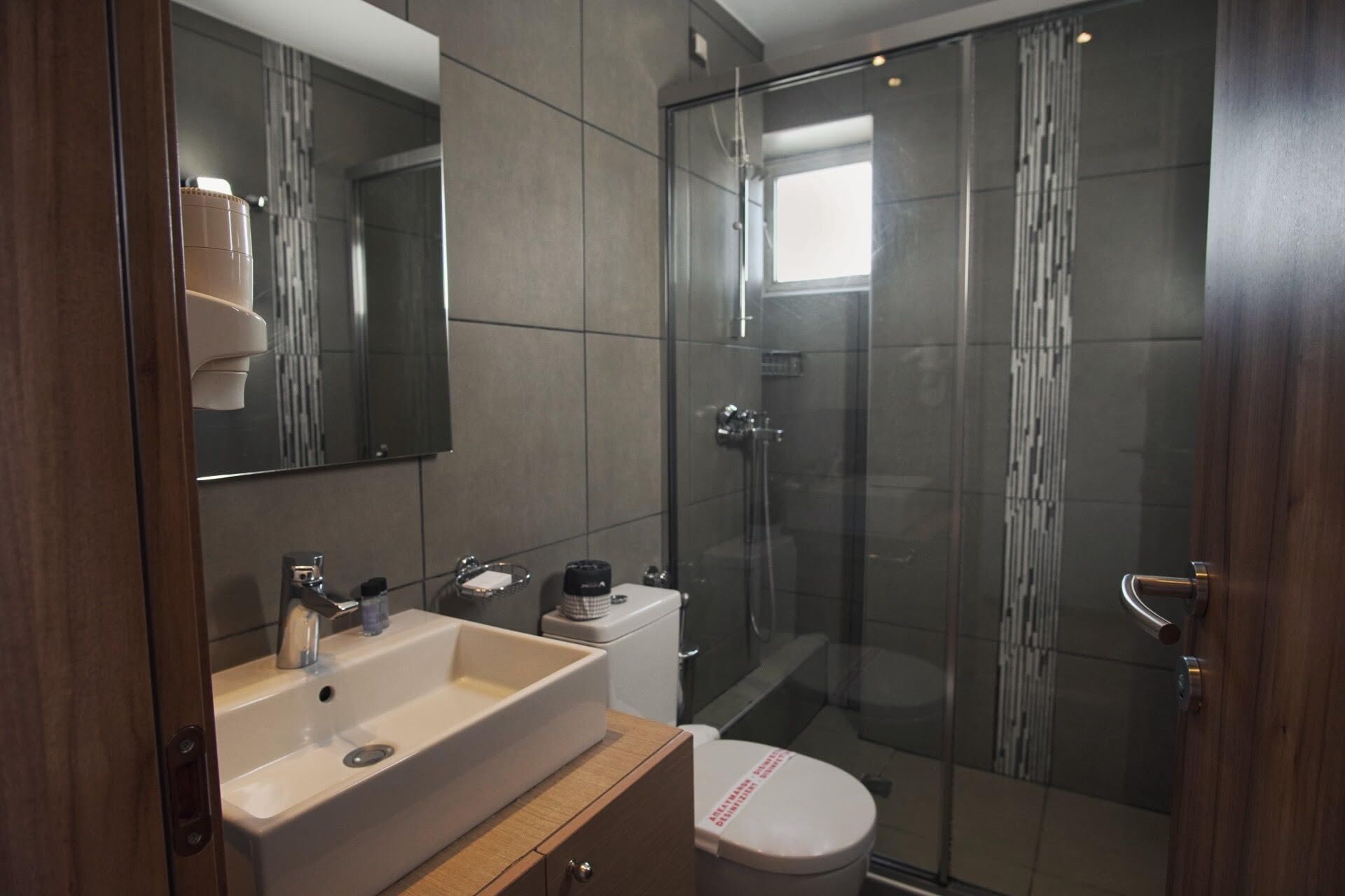 A modern bathroom with a large mirror, two sinks, a toilet, and a glass-enclosed shower.