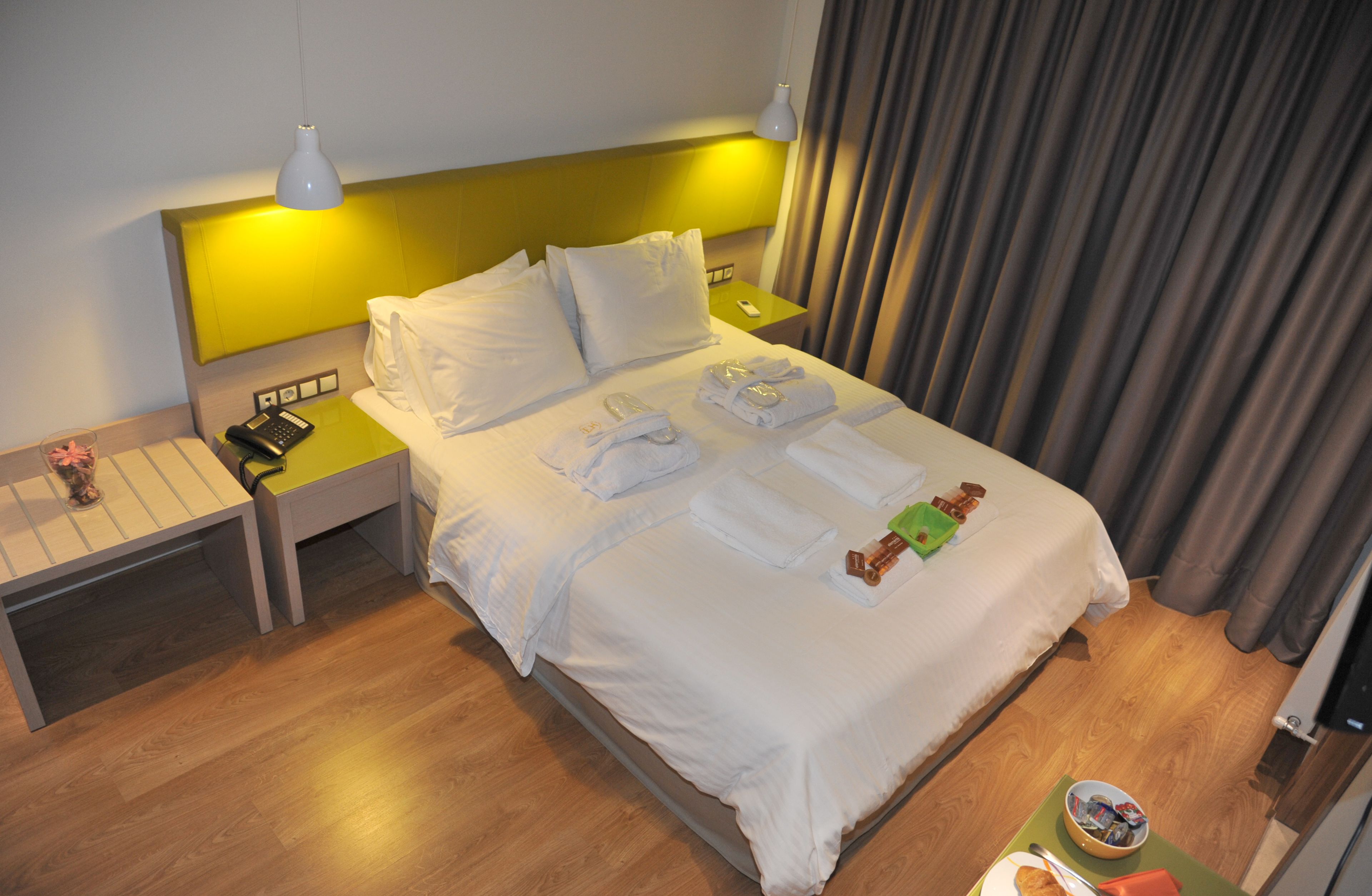 A hotel room with a neatly made bed, a bedside table with a lamp, and a nightstand with a phone and remote control.