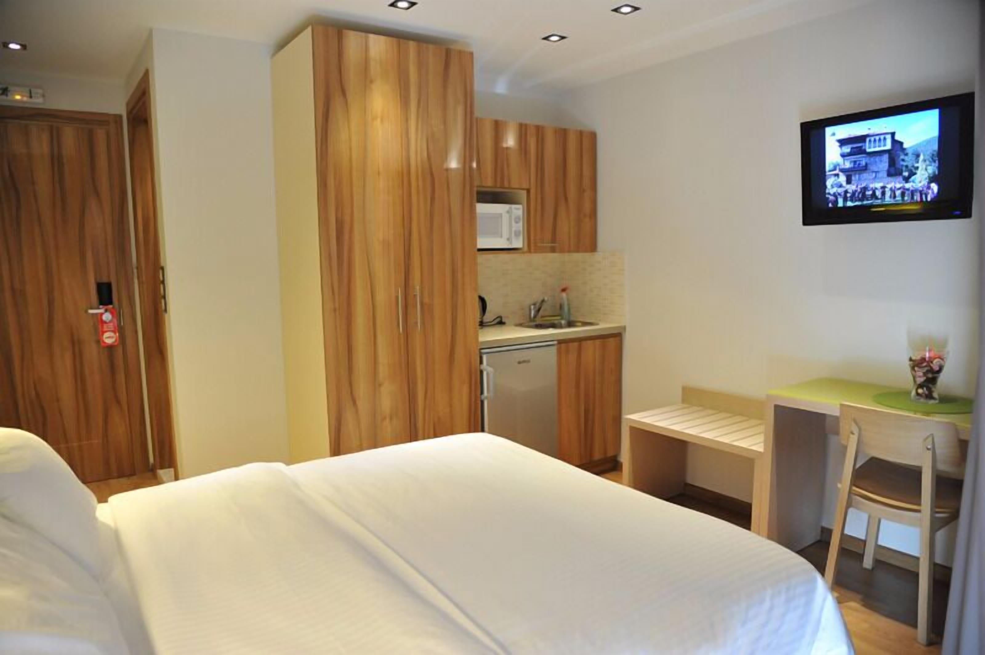 Une chambre d’hôtel comprenant un lit, une kitchenette, un téléviseur fixé au mur et un bureau avec une chaise.