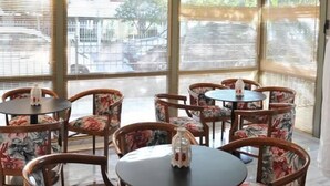 A dining area with round tables and floral-patterned chairs, large windows with blinds, and a view of the outside. - Elements Rooms and Apartments (Chalandri)