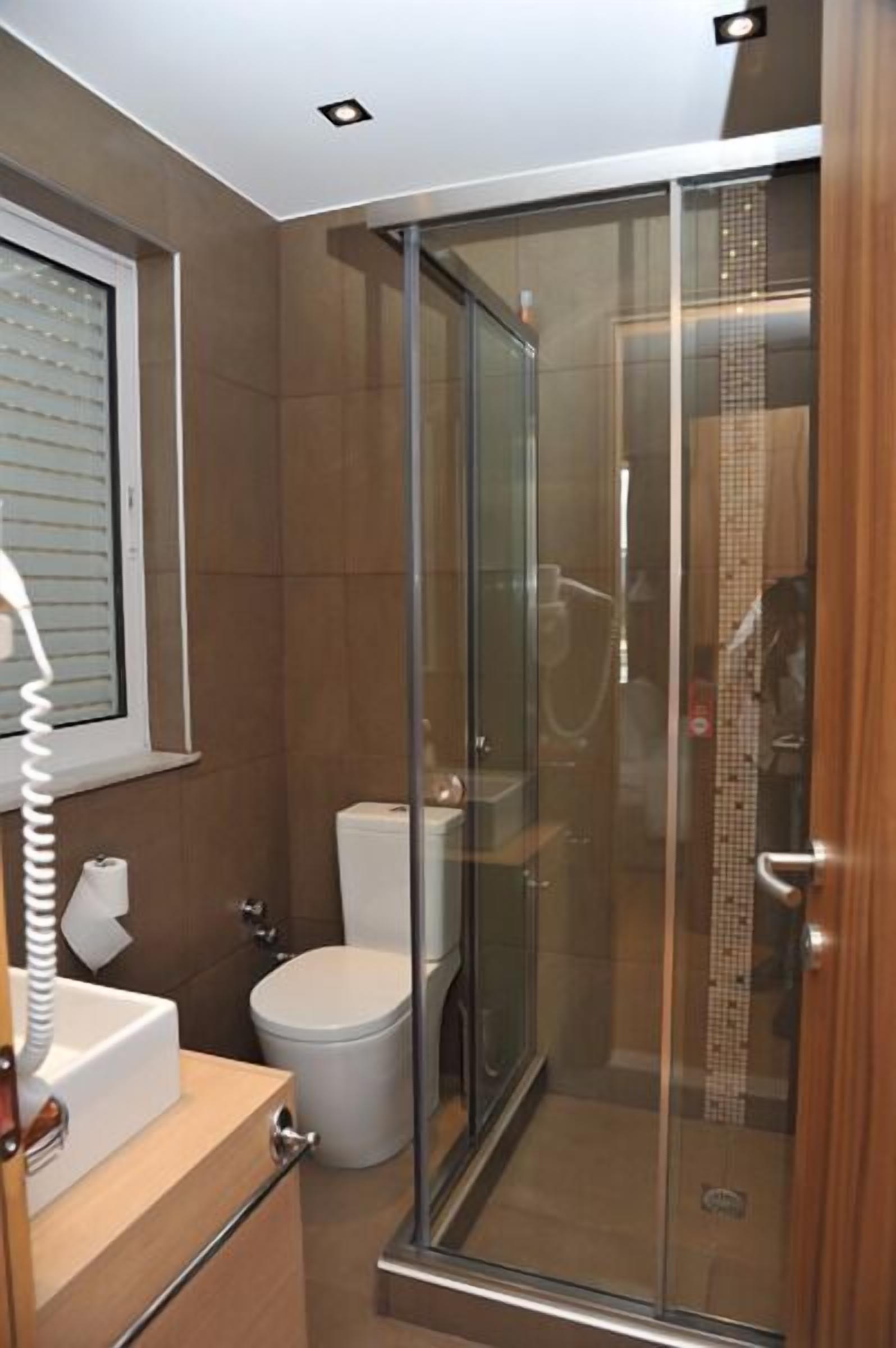 A modern bathroom with a glass shower enclosure, a toilet, and a sink with a mirror.