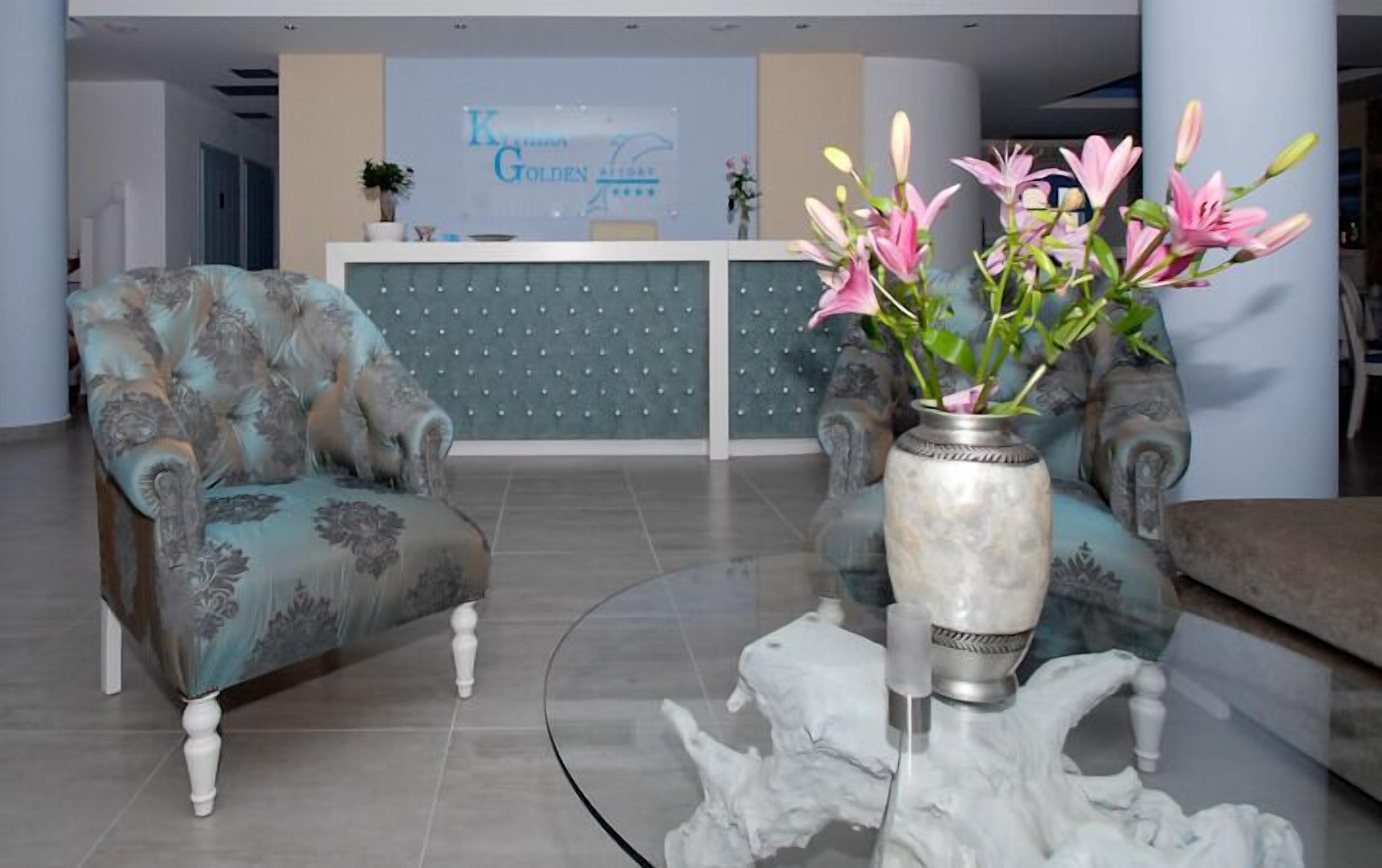 A reception area with a reception desk, two upholstered armchairs, and a vase with flowers on a glass table.