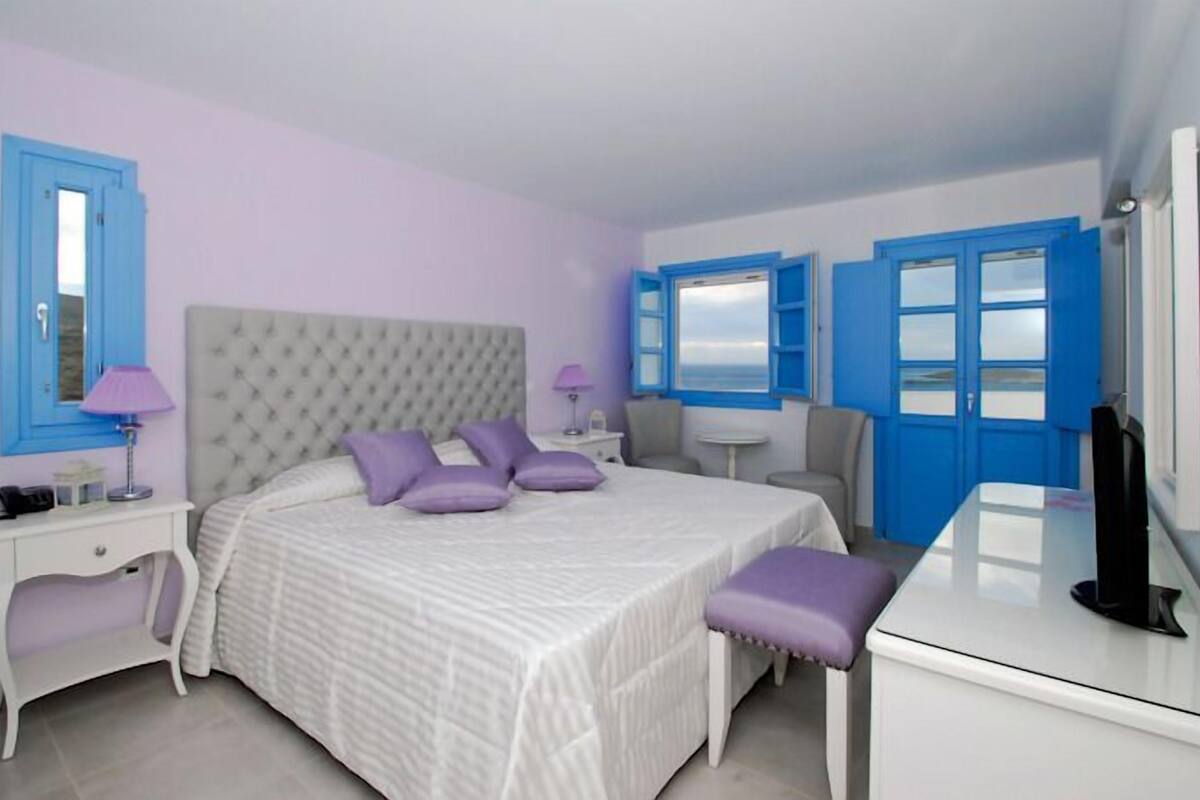 A bedroom with a large bed, two nightstands, a dresser, and a window with blue shutters.