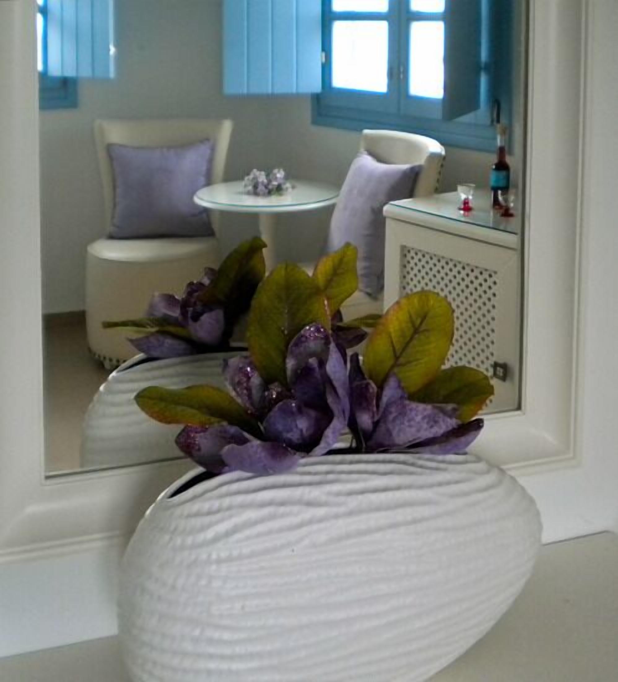 A white vase with purple flowers on a white surface.