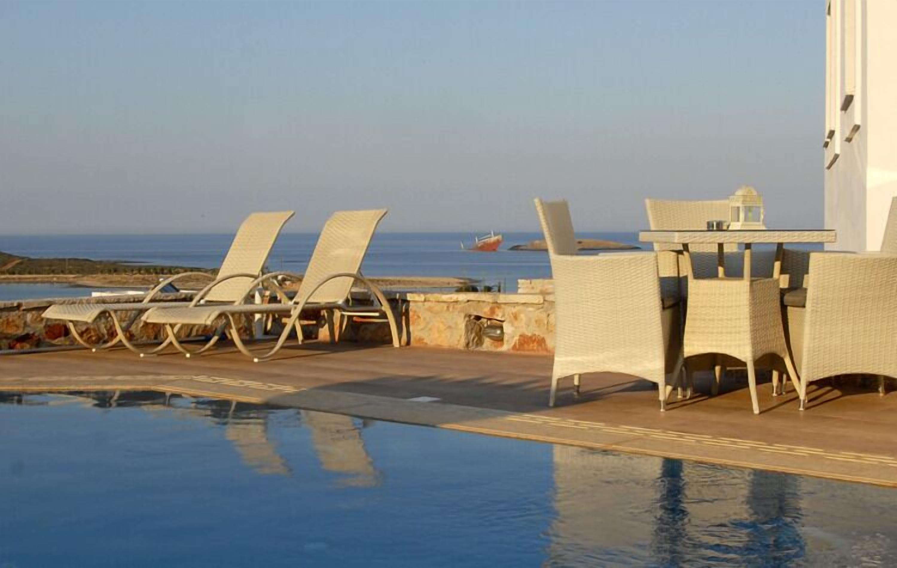 Ein Poolbereich mit Liegestühlen und einem Tisch, mit Blick auf das Meer.