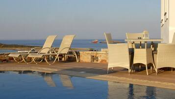 Ein Poolbereich mit Liegestühlen und einem Tisch, mit Blick auf das Meer.