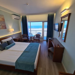 A hotel room with a bed, a desk, a chair, and a large window with a view of the beach. - Comandor (Constanta)