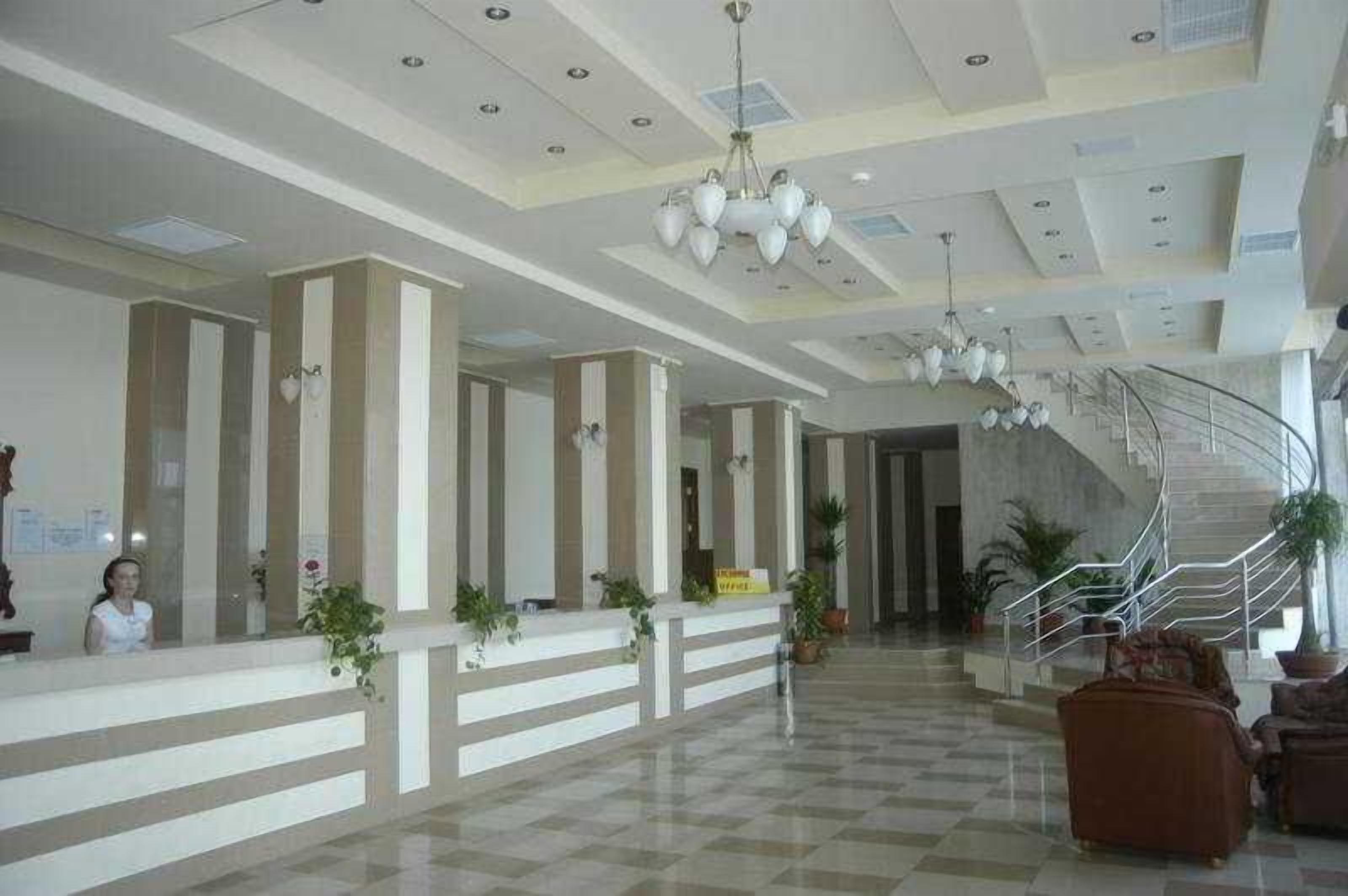 A hotel lobby with a reception desk, a staircase, and potted plants.