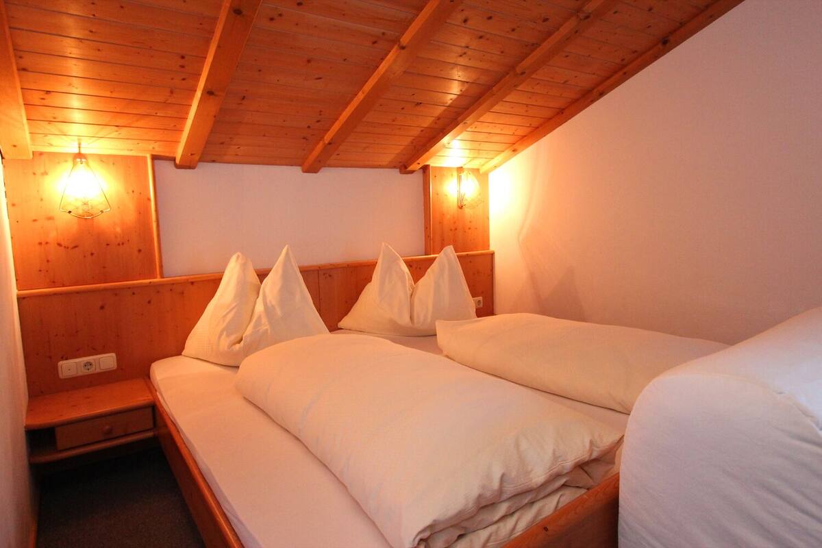 Ein gemütliches Zimmer mit Holzbalkendecke, zwei Betten mit weißen Bettwäsche und Wandleuchten.