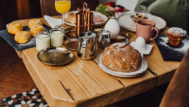 A wooden dining table with breakfast items including pastries, a loaf of bread, and a glass of orange juice.
