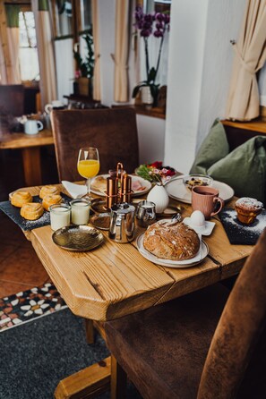 A wooden dining table with breakfast items including pastries, a loaf of bread, and a glass of orange juice. - Pension Forsthof (Sankt Johann im Pongau)