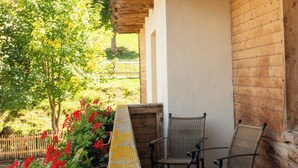 A wooden balcony with two wicker chairs, a wooden bench, and red flowers.