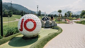 A golf course with a large golf ball sculpture, a fenced area, and a paved walkway.
