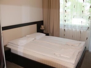 A neatly made bed with white linens, a dark headboard, and a bedside lamp on a nightstand. - Hotel Siret Mamaia (Constanta)