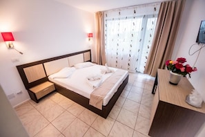 A hotel room with a bed, a nightstand, a TV, and a window with curtains. - Hotel Siret Mamaia (Constanta)