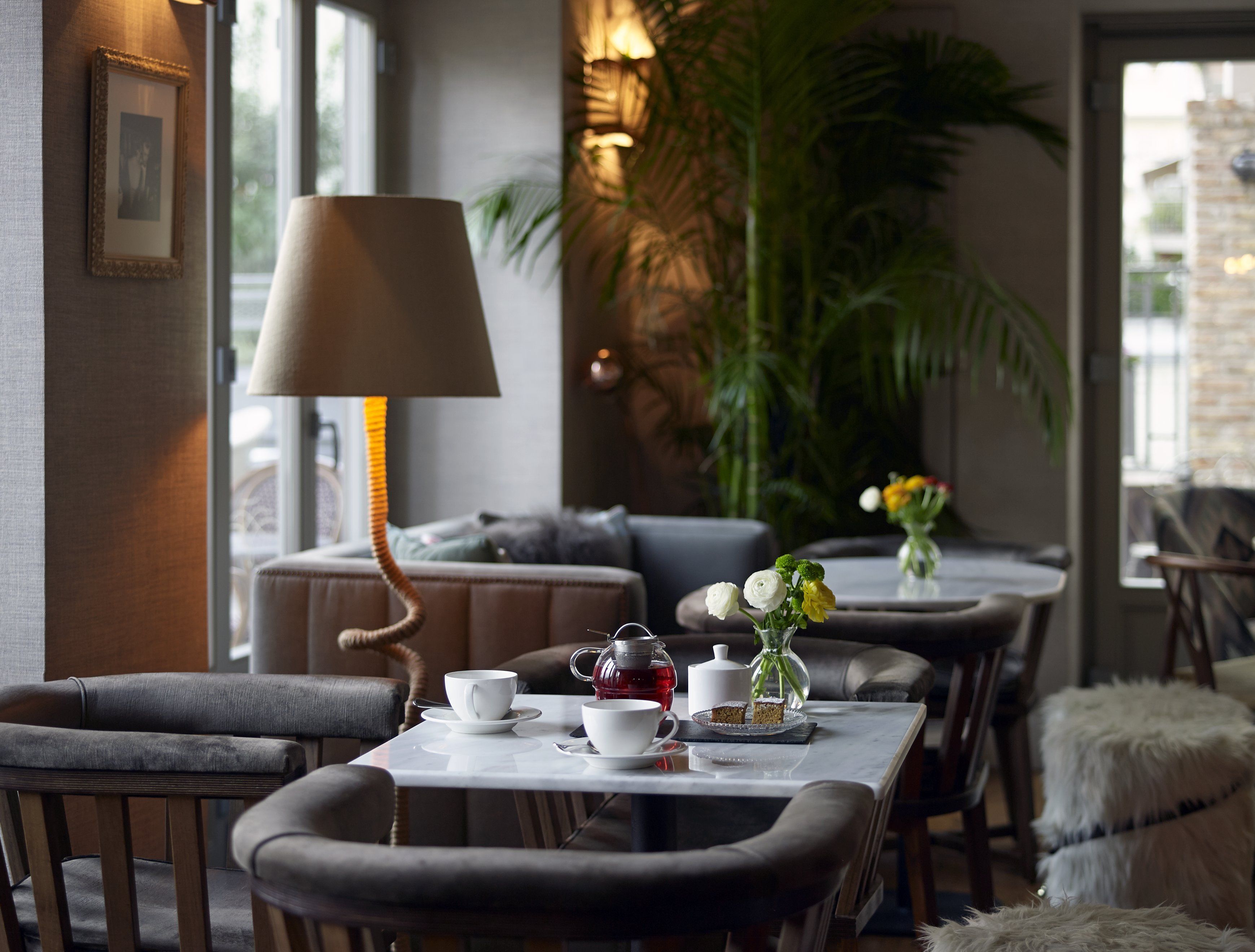A cozy dining area with a table set for two, featuring a lamp, a vase with flowers, and a teapot.