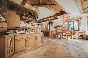 A spacious kitchen with wooden cabinets, a dining area with a large table and chairs, and a view of the outdoors through a window. - Wieshof Apartments (Sankt Johann im Pongau)
