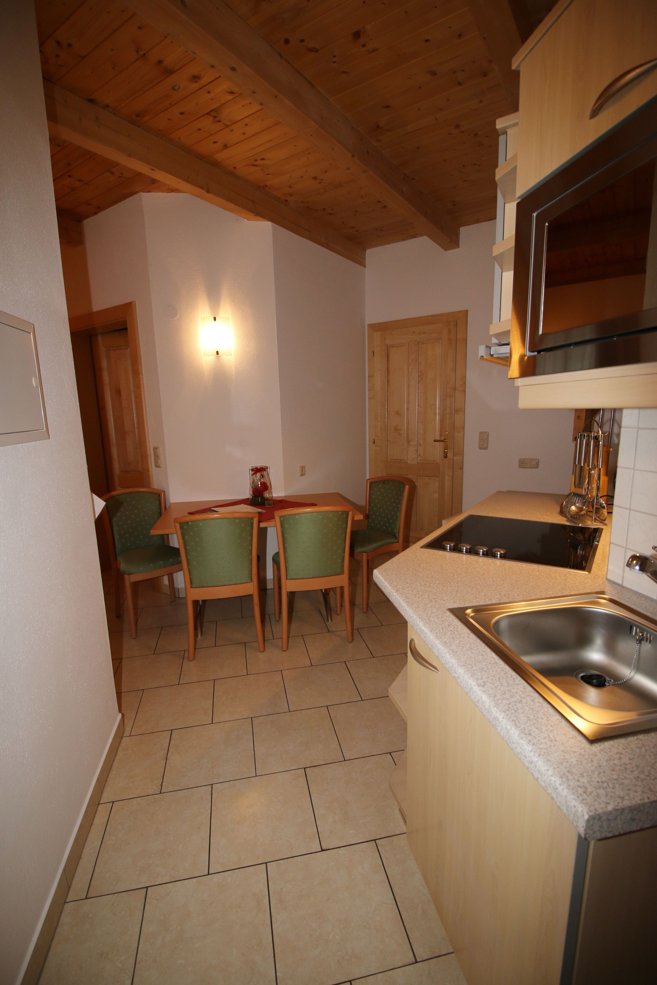 A compact kitchen with a wooden ceiling, a built-in stove, and a sink. There is a dining area with a table and chairs.