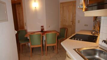A compact kitchen with a wooden ceiling, a built-in stove, and a sink. There is a dining area with a table and chairs.