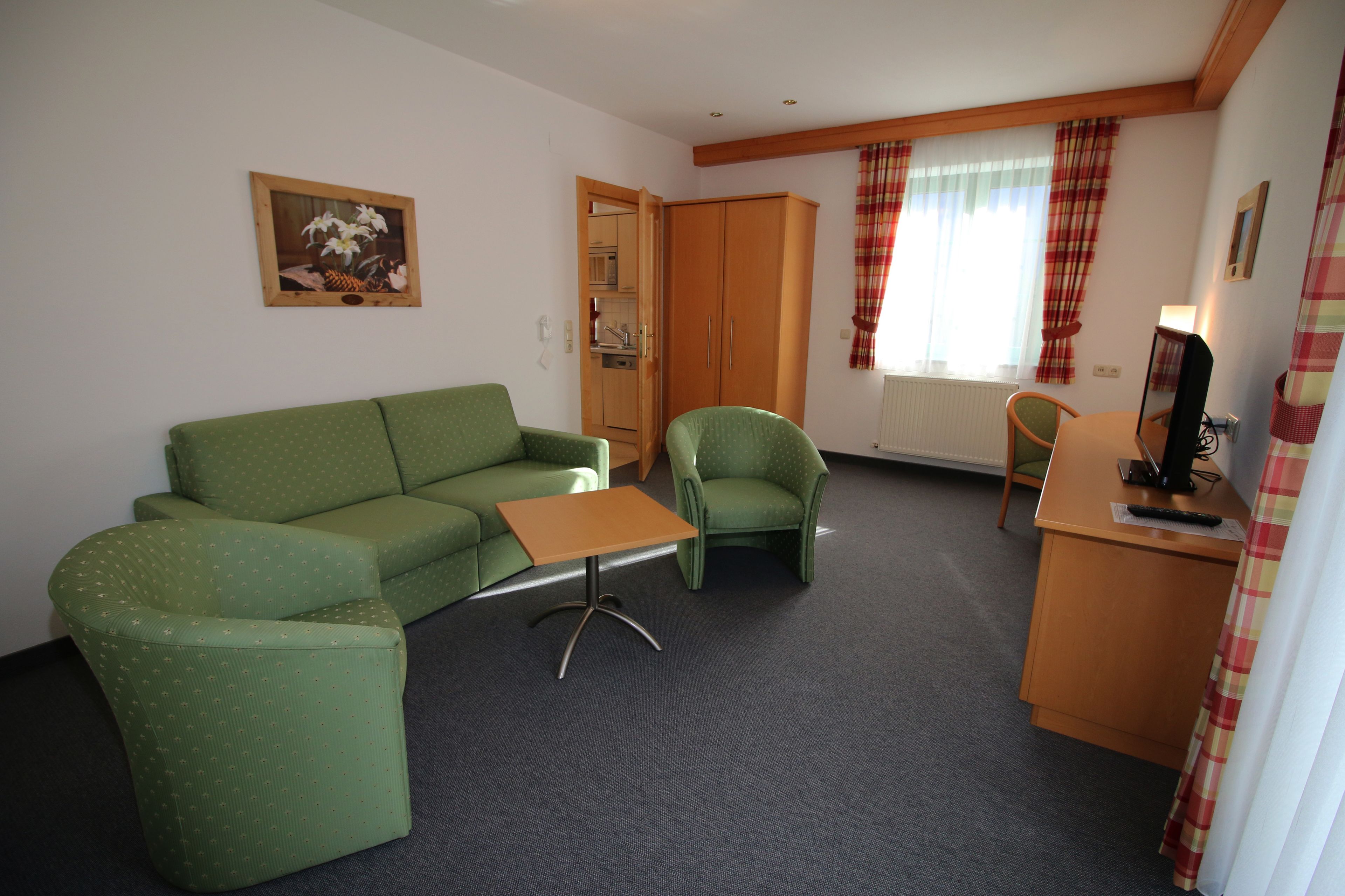 Ein Zimmer mit einem grünen Sofa, einem grünen Sessel, einem kleinen Holztisch und einem Holzbüro mit einem Computer.