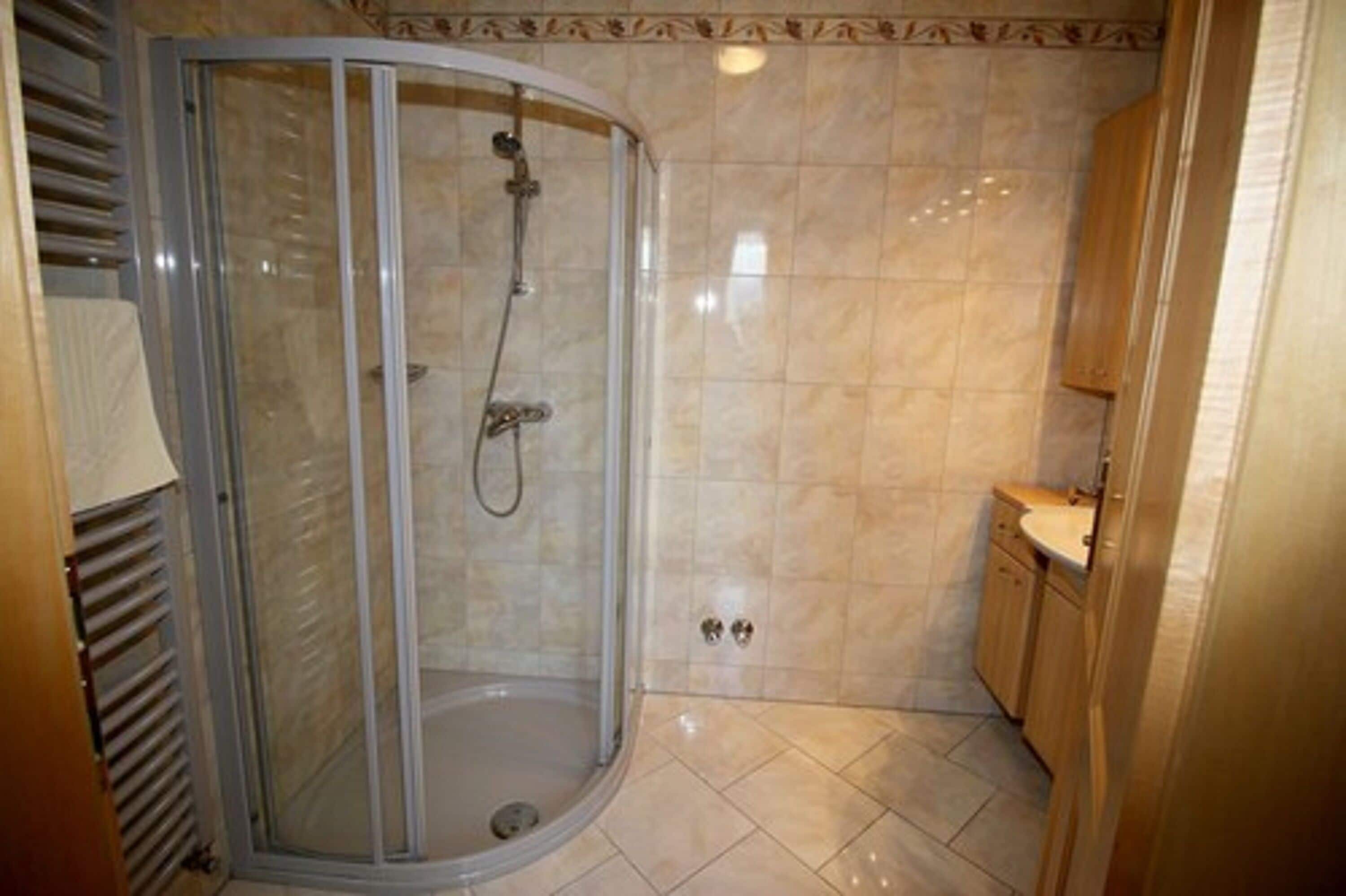 Um chuveiro com porta de vidro, piso ladrilhado e armário de madeira.