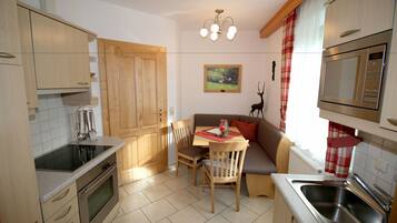 A compact kitchen with wooden cabinets, a built-in oven, a dining table with chairs, a red and white checkered curtain, and a painting on the wall.