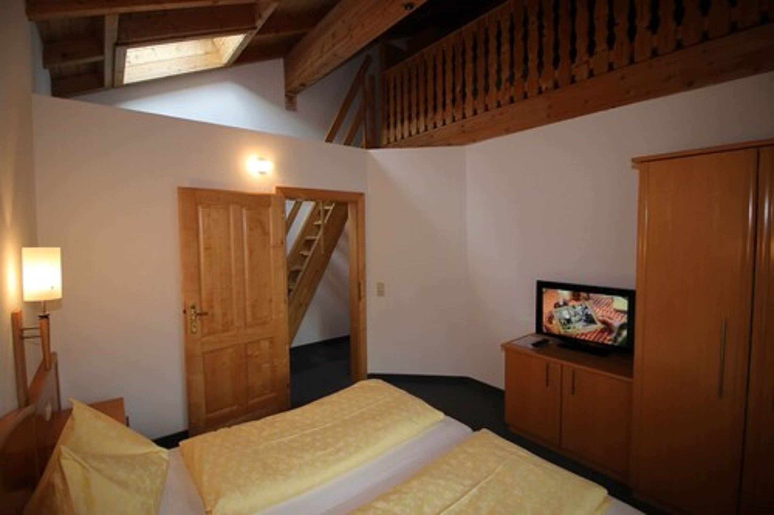 A bedroom with two beds, a wooden wardrobe, a television, and a staircase.