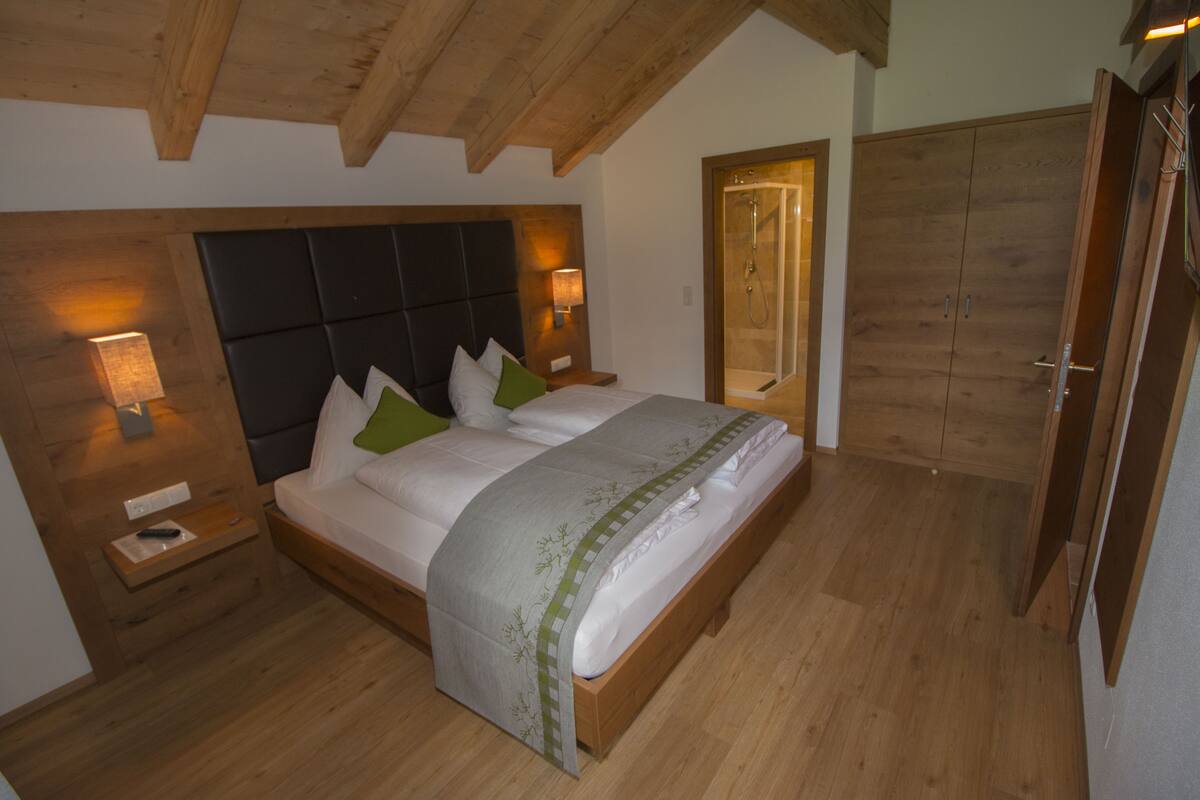 A bedroom with a wooden headboard, a large bed with pillows, bedside lamps, and a wooden wardrobe.