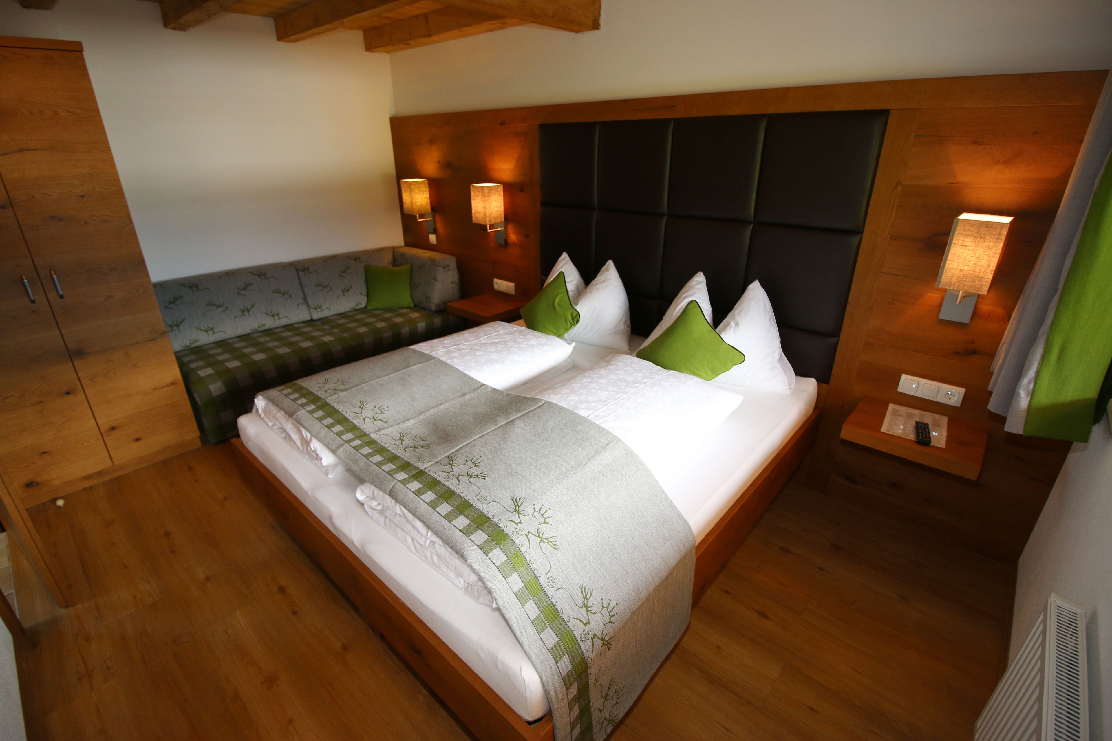 A bedroom with a bed, wooden headboard, bedside lamps, a bench, and a wardrobe.