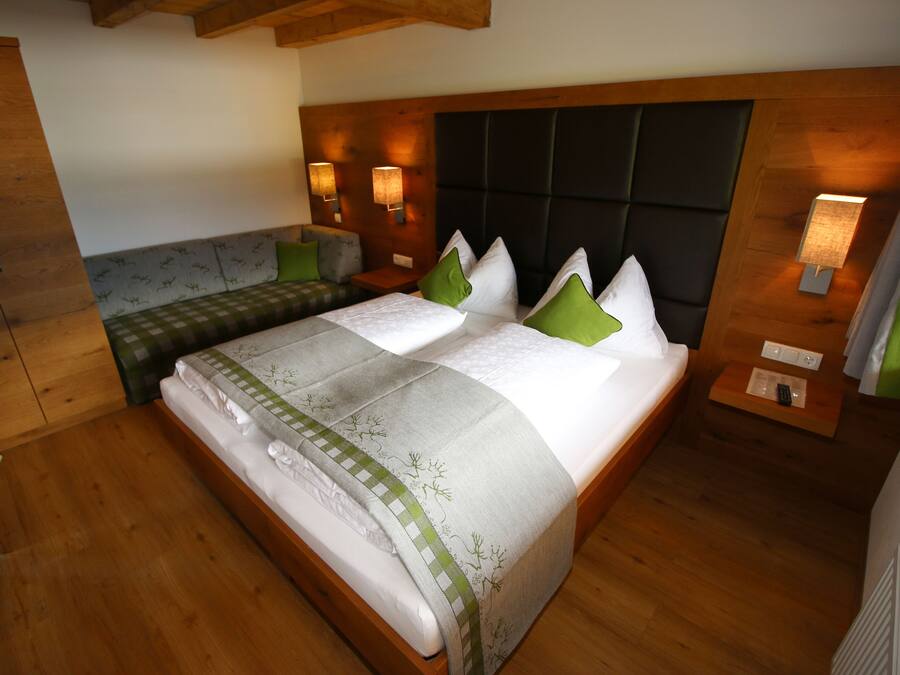 A bedroom with a bed, wooden headboard, bedside lamps, a bench, and a wardrobe.