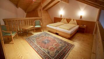 A cozy attic bedroom with a wooden floor, a bed with pillows, a nightstand, a chair, and a decorative rug.