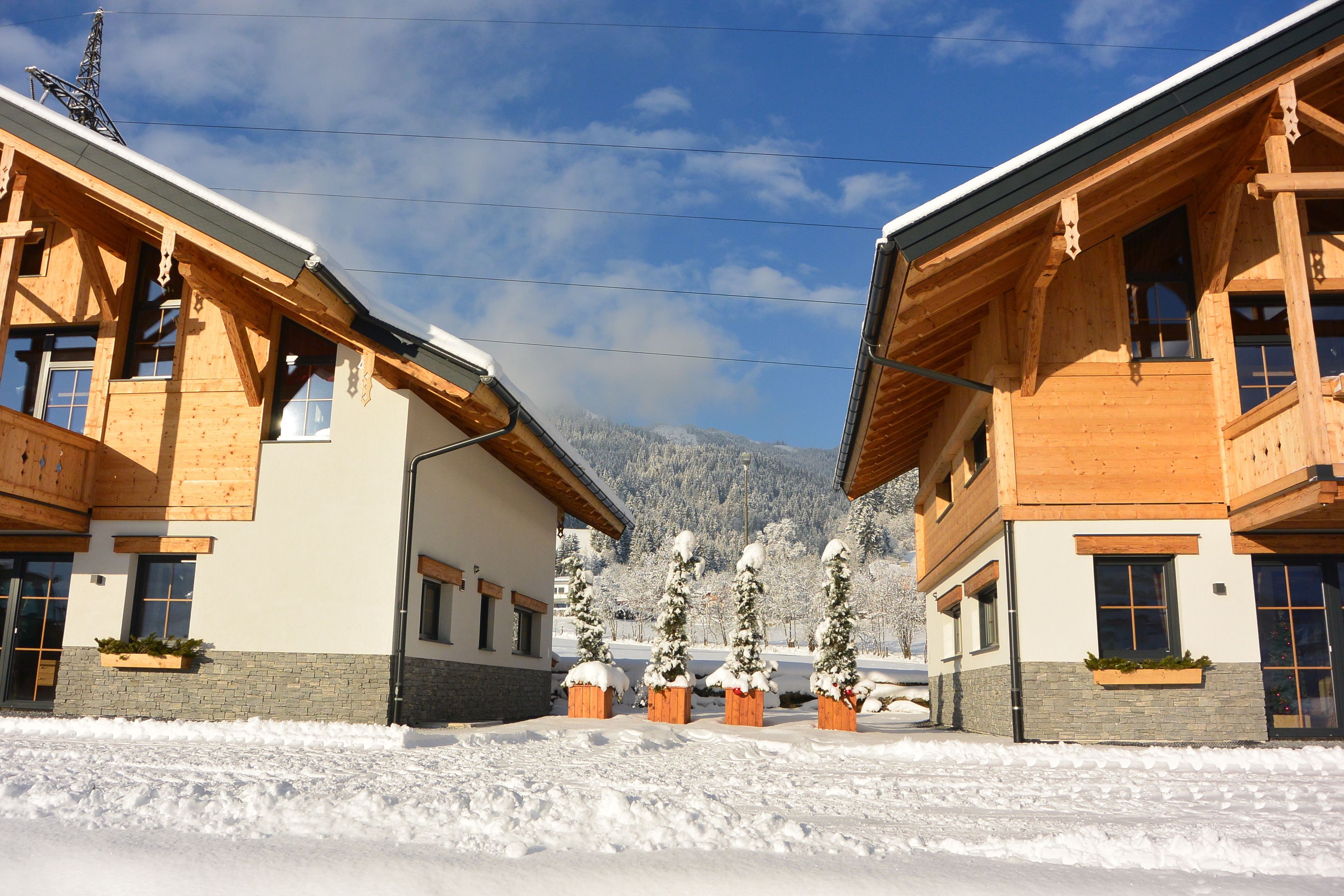 A modern wooden building with a snow-covered landscape and mountains in the background.
