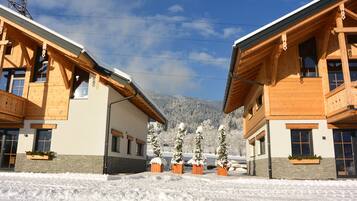 A modern wooden building with a snow-covered landscape and mountains in the background.