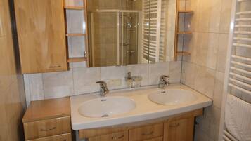 A bathroom with two sinks, a mirror, and a shower.
