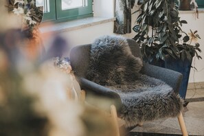 Une chaise dotée d’un siège et d’un dossier recouverts de fourrure, placée près d’une fenêtre donnant sur une plante à l’extérieur.